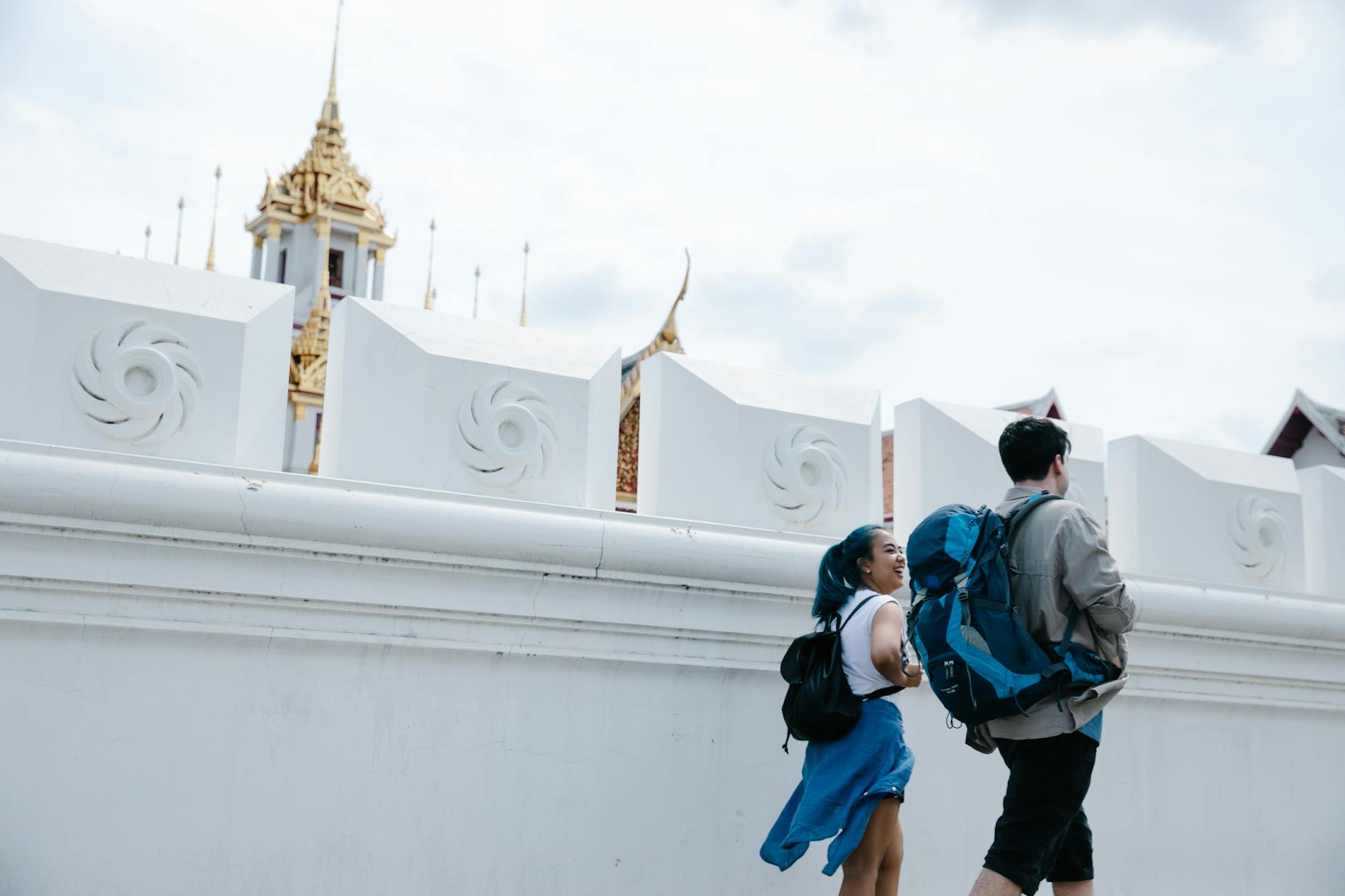 Dwóch turystów idzie przy białym murze w Bangkoku, w tle złota wieża świątyni