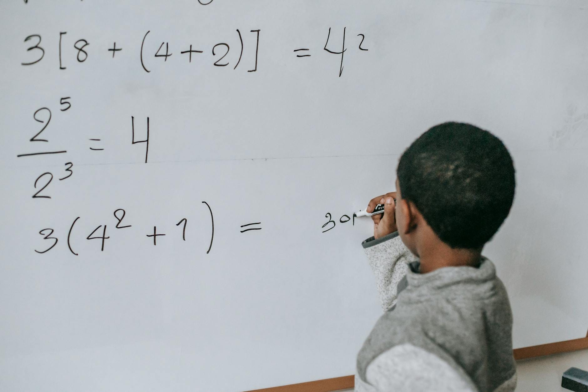Chłopiec pisze działania matematyczne na białej tablicy w klasie