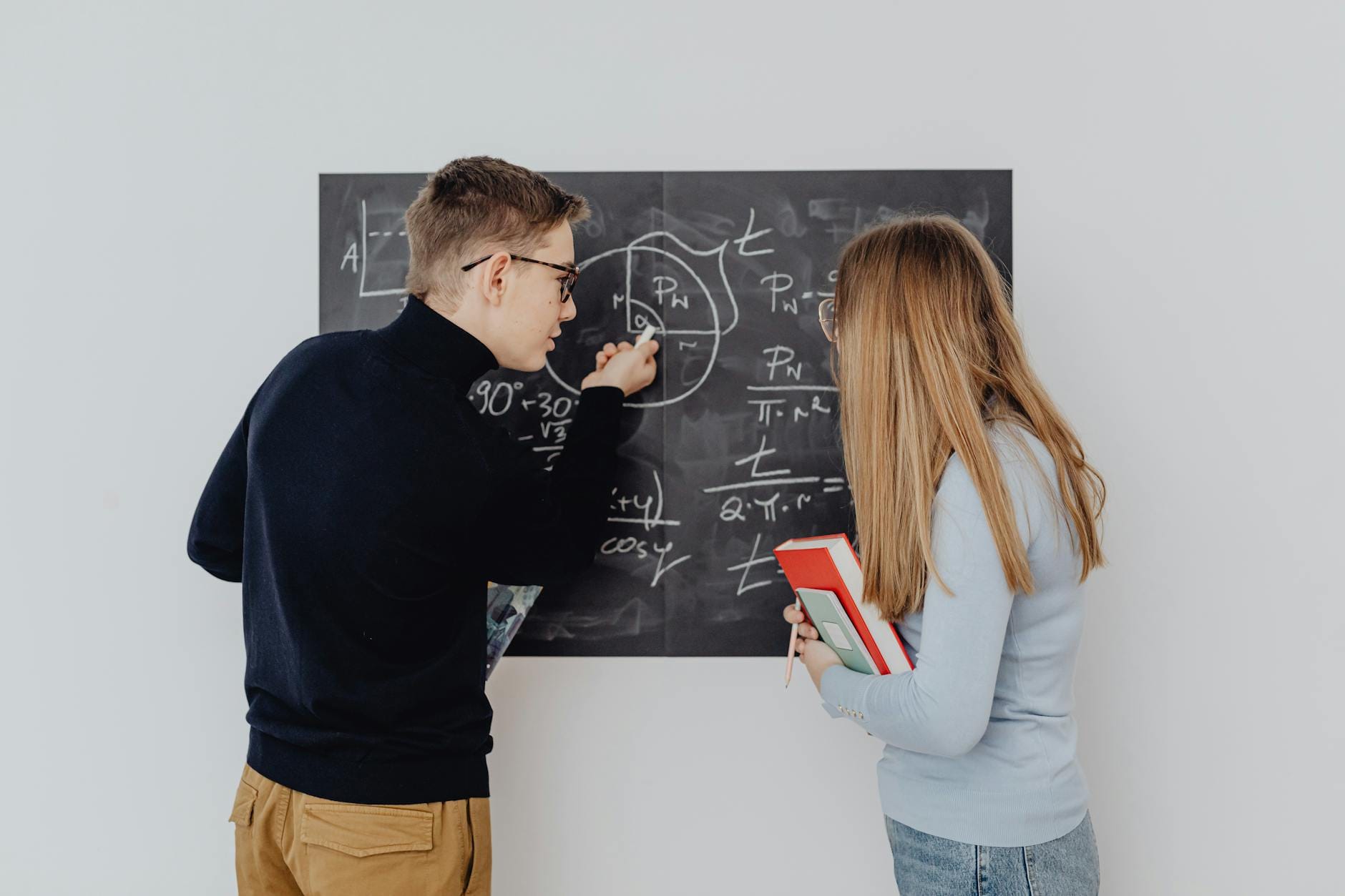 Dwóch studentów przy tablicy z równaniami, wspólne rozwiązywanie zadań