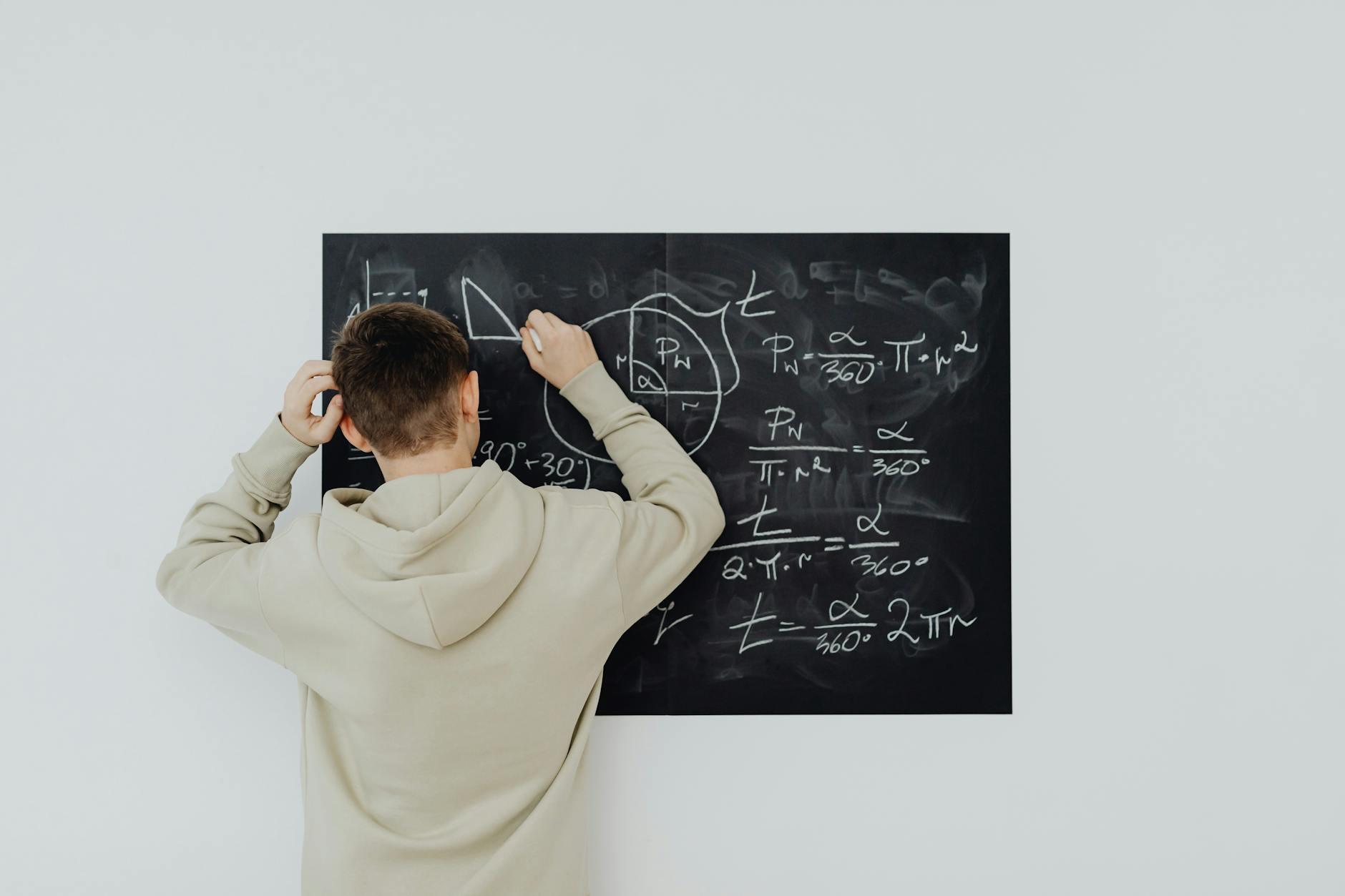 Nastolatek w bluzie zapisuje na tablicy skomplikowane wzory matematyczne