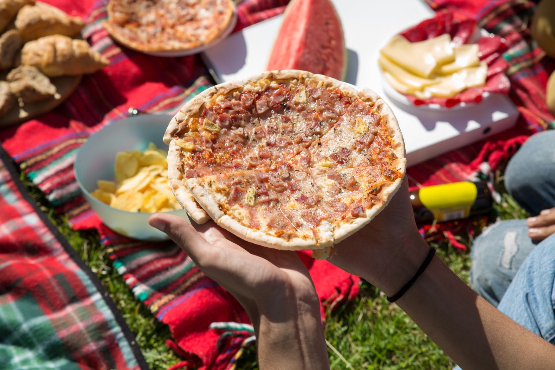 Goście na pikniku plenerowym trzymają kawałki pizzy w słońcu