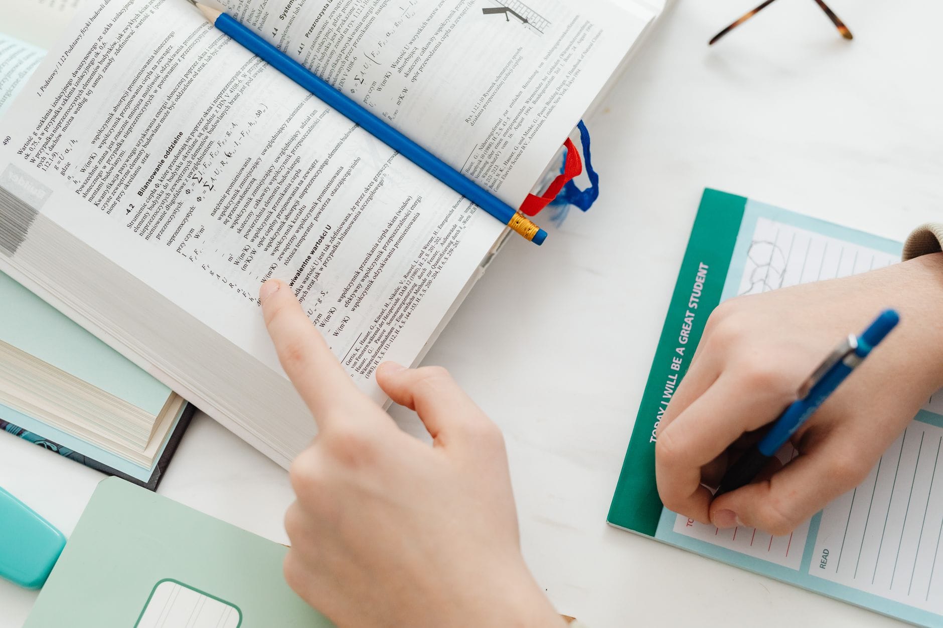 Uczeń pochylony nad otwartym podręcznikiem z matematyki i notatkami