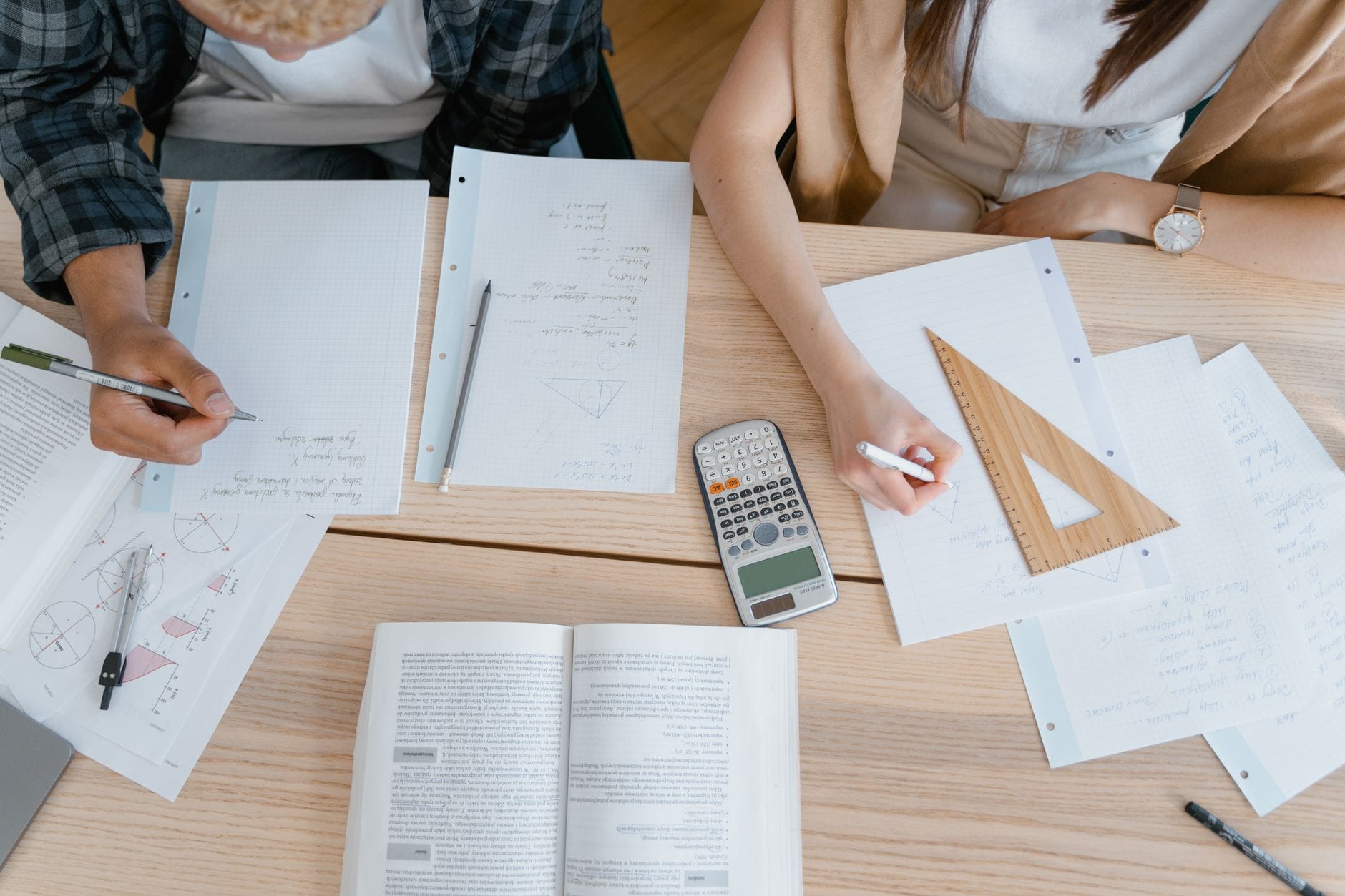 Uczniowie liczą zadania z matematyki przy biurku z zeszytami i kalkulatorem