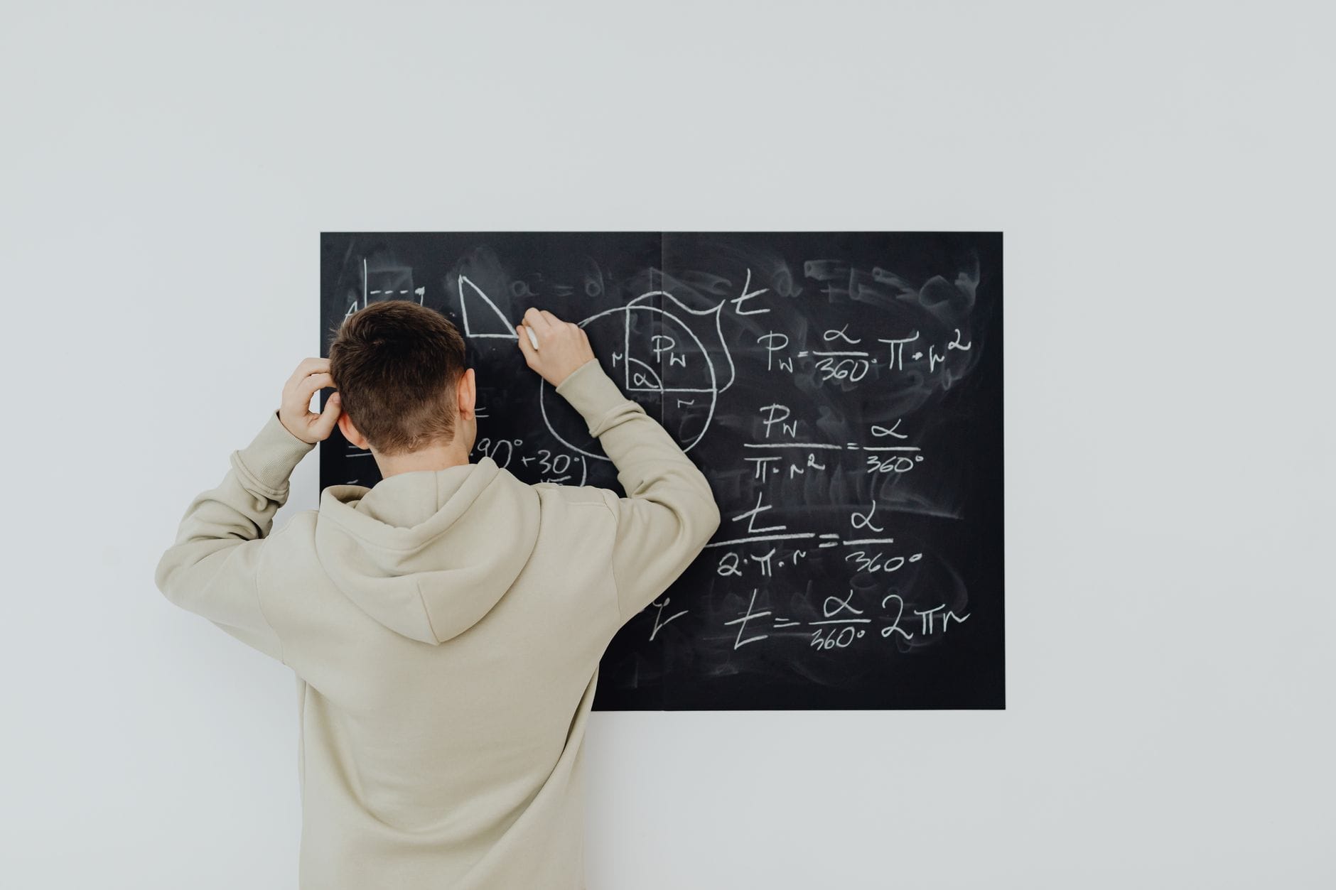 Nastolatek w bluzie pisze wzory algebraiczne na tablicy w klasie