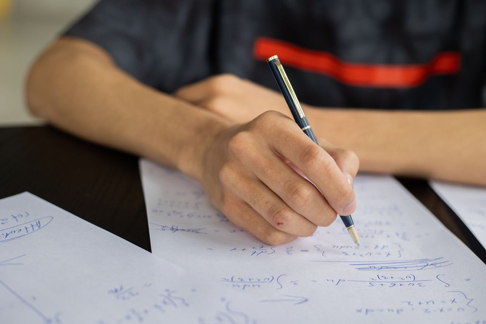Uczeń przy biurku zapisuje wzory matematyczne na kartce Uczeń przy biurku zapisuje wzory matematyczne na kartce